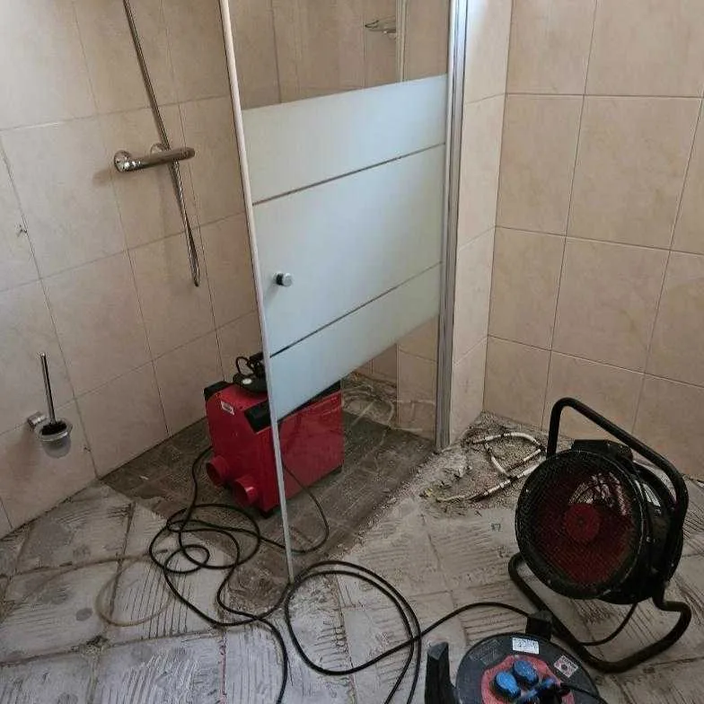 Badkamer met opengebroken vloer en bouwdrogers na een lekkage