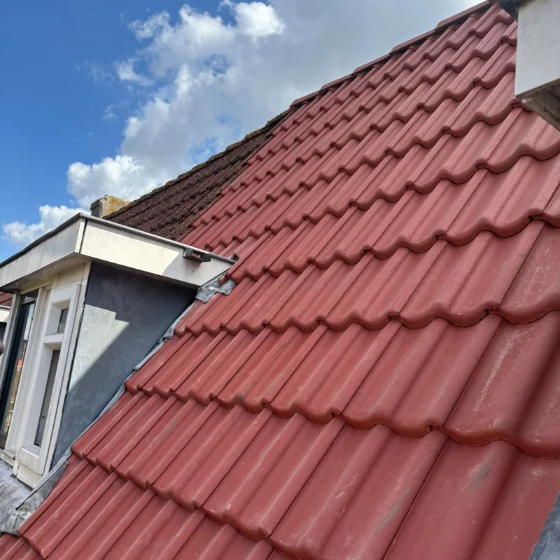 Hellend dak met nieuwe rode dakpannen naast een dakkapel