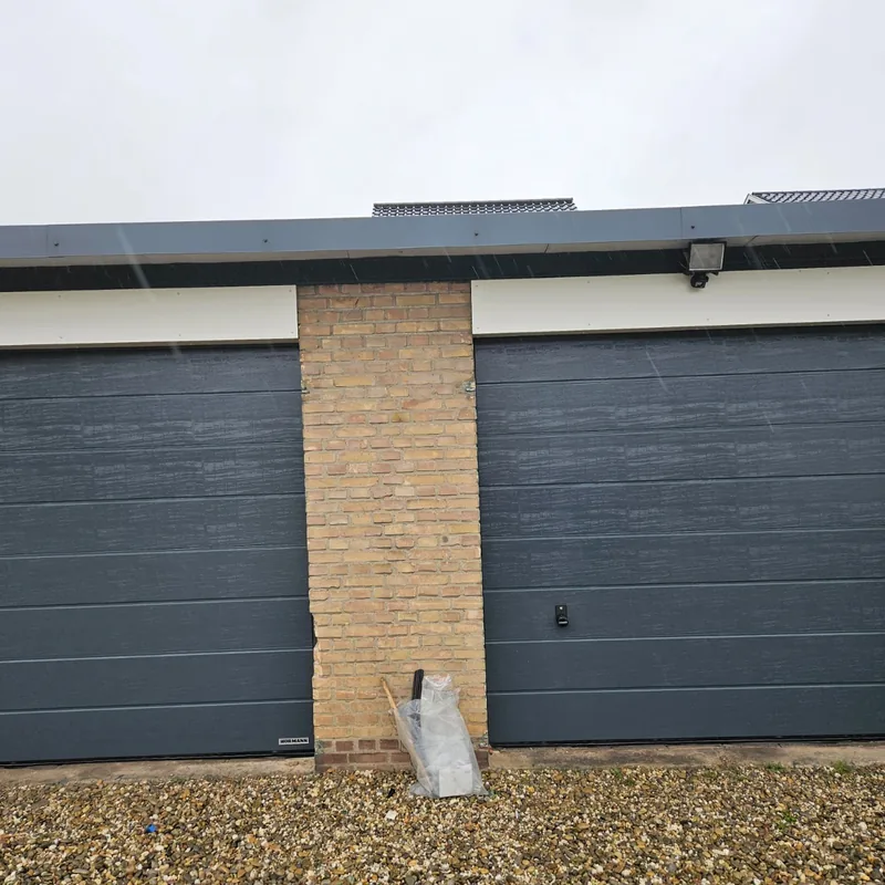 Twee nieuwe grijze garagedeuren in een rij garages