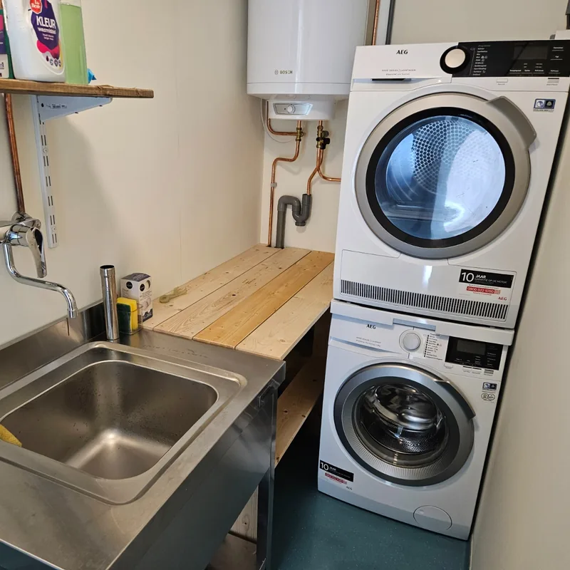 Wasruimte met boiler, koperen leidingen, spoelbak en aansluitingen voor wasmachine en droger